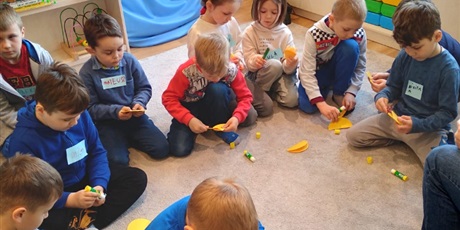 Powiększ grafikę: Dzieci siedzą na dywanie z żółtymi kołkami z papieru i robią kurczaka. 